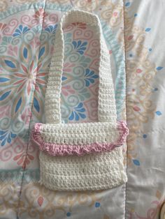 a white crocheted purse laying on top of a pink and blue flowered blanket