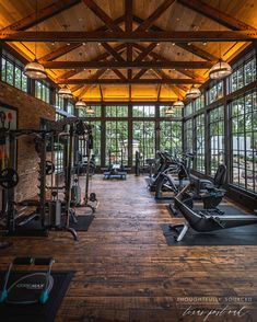 an indoor gym with lots of machines and windows on the wall, along with wood flooring