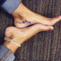 two feet with mountains tattooed on them sitting next to eachother's legs