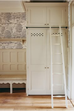 an empty room with white closets and wooden flooring on the side, along with a ladder leading up to it