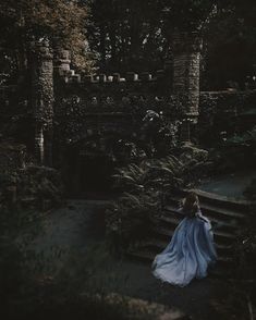 a woman in a blue dress is walking down the stairs to an old castle like building