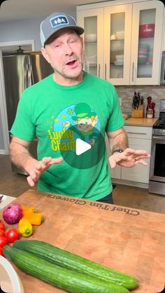 a man standing in front of a cutting board with cucumbers and tomatoes on it