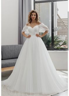 a woman standing in front of a window wearing a white wedding dress with puffy sleeves