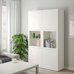 a living room filled with white furniture and a potted plant on top of a table