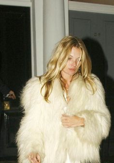 a woman in a white fur coat is walking