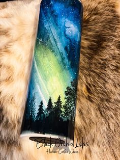 a phone case painted with the aurora bore and stars in the night sky, sitting on a furry surface