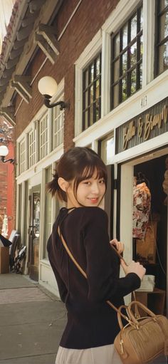 a woman standing in front of a store holding onto a brown purse and smiling at the camera