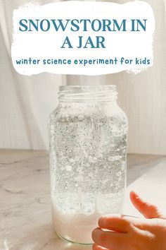 a jar filled with snow sitting on top of a table next to a person's hand