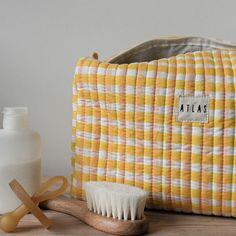 a yellow and white checkered cosmetic bag next to a wooden brush on a table