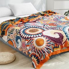 a bed covered in a colorful blanket next to pillows and a basket on the floor