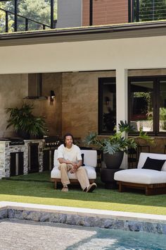 a man sitting on a chair in front of a house with a pool and patio furniture