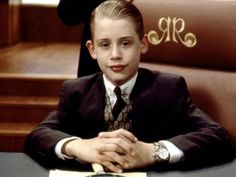 a boy in a suit sitting at a desk with his hands folded over the table