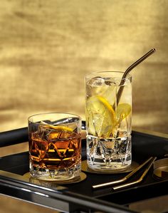 a tray with two glasses filled with drinks and silverware next to each other on top of a table