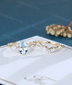 two gold rings with blue topazte and white diamonds on a table next to dried flowers