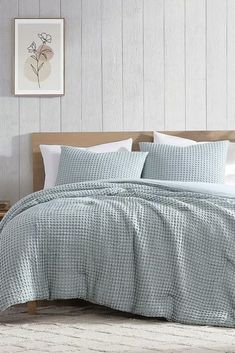 a bed with blue and white comforter in a bedroom next to a painting on the wall