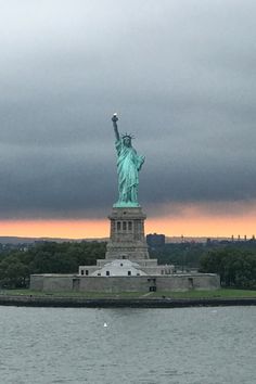 the statue of liberty stands in front of a body of water under a cloudy sky