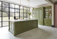 a large kitchen with green cabinets and marble counter tops, along with an island in the middle