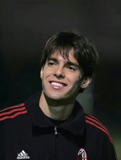 a young man smiling at the camera with his hair pulled back and wearing a black shirt