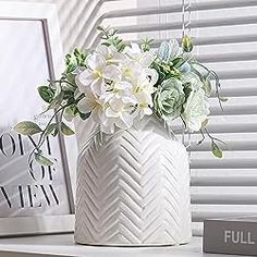 a white vase filled with flowers sitting on top of a table next to a window