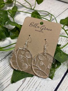 a pair of earrings sitting on top of a wooden table next to green leafy plants