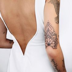 a woman's arm with tattoos on it and a white tank top behind her