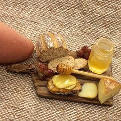 a wooden board topped with bread and cheese next to a jar of honey on top of a table