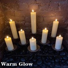 seven white candles are lit in a dark room with the words warm glow above them