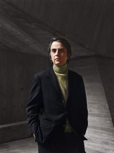 a man in a black suit and turtle neck sweater standing with his hands in his pockets