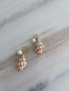 A pair of shell earrings with gold details and a hanging pearl perfect for the summer Shell Pearl Earrings, Shell-shaped Pearl Earrings With Pearl Charm, Pearl Shell Earrings With Pearl Charm, Pearl Shell Drop Earrings With Pearl Drop Detail, Gold Shell Dangle Earrings, Pearl Drop Shell-shaped Earrings In Mother Of Pearl, Pearl Charm Drop Earrings In Mother Of Pearl, Ocean-inspired Pearl Shell With Pearl Drop, Ocean-inspired Pearl Drop Shell