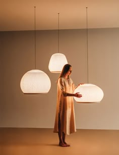 a woman is standing in front of three lamps that are hanging from the ceiling above her