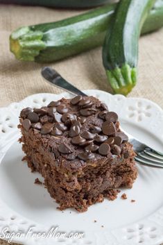 a piece of chocolate cake on a plate with a fork and cucumbers in the background