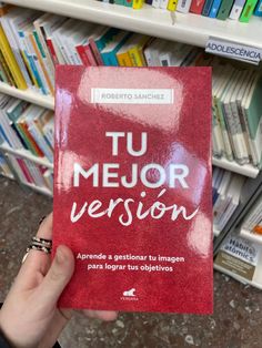 a person holding up a red book in front of a bookshelf