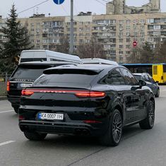 a black porsche cayen is driving down the street in front of other cars and buses