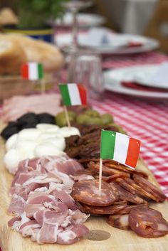 an assortment of meats and cheeses on a wooden platter with italian flags