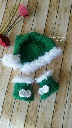 a crocheted hat and booties are sitting on a wooden floor next to flowers