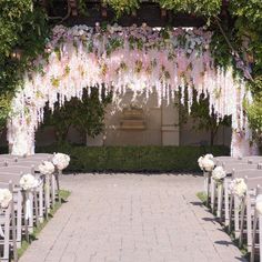 an outdoor ceremony setup with white and pink flowers on the aisle, surrounded by greenery