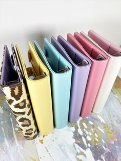 five different colored leather cases are lined up in a row on a surface with paint splotters