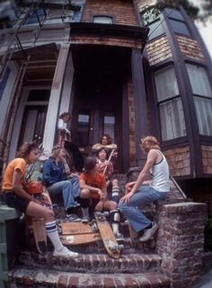 a group of young men sitting on steps in front of a house with skateboards