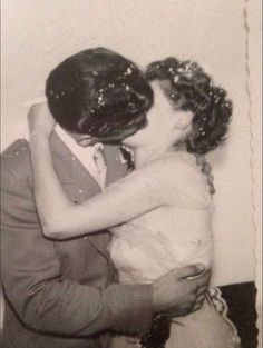 an old black and white photo of two people hugging each other in front of a wall