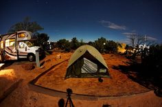 a camper trailer parked next to a camping tent at night with the lights on