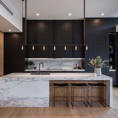 a kitchen with black cabinets and marble counter tops, two stools at the island