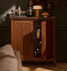 a wooden cabinet with wine bottles and glasses on it next to a couch in a living room