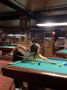 a woman leaning over a pool table in a room filled with tables and people playing billiards