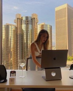 a woman sitting at a table with a laptop in front of her and a glass of wine