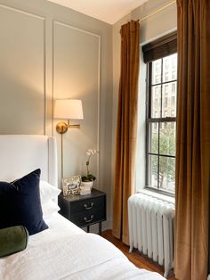 a white bed sitting next to a window in a room with curtains on the windowsill