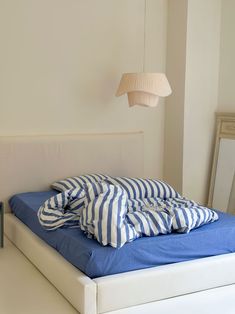 a bed with blue and white sheets on top of it next to a wall light