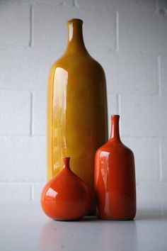 two orange vases sitting next to each other on a white counter top in front of a brick wall