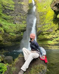 a man sitting on top of a rock next to a waterfall