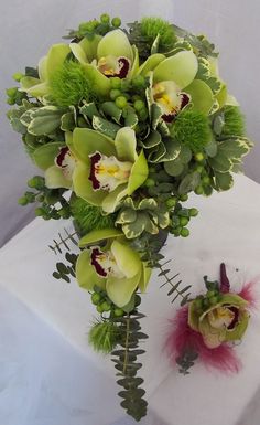 a bouquet of flowers sitting on top of a table next to a vase with greenery