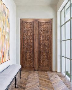 a large wooden door sitting in the middle of a room next to a bench and windows